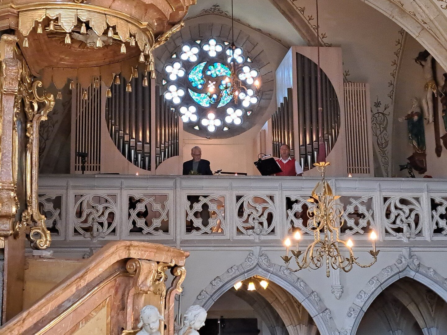 Organisten spielen in der Empore einer Kirche vor einer Rosette und einer Orgel.