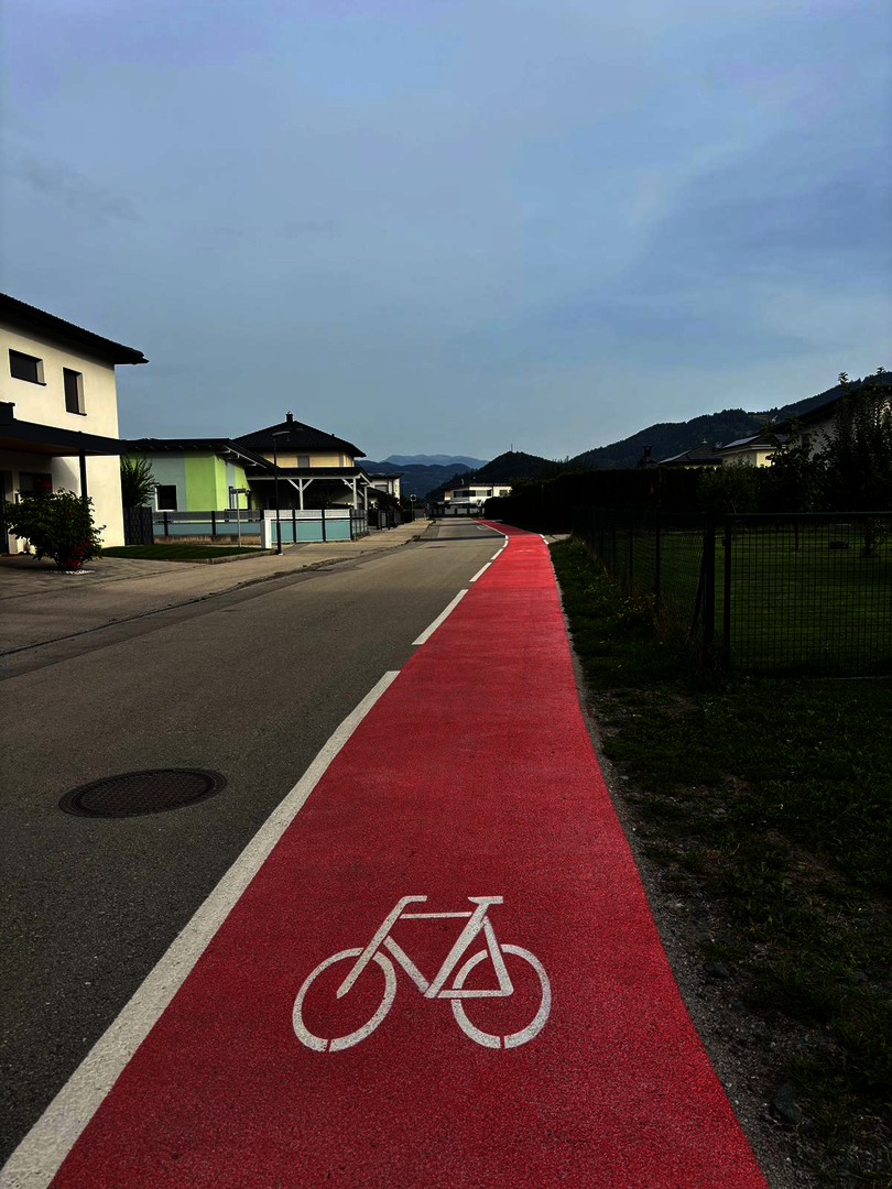 Radweg mit Fahrradsymbol in Österreich führt durch eine Siedlung mit Häusern und Bergen